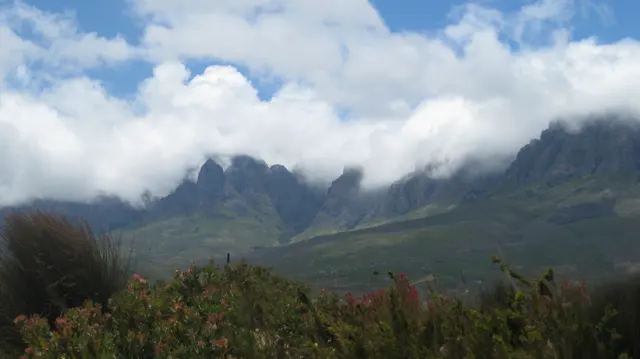 Cloud flows over steep peaks above dark green slopes.