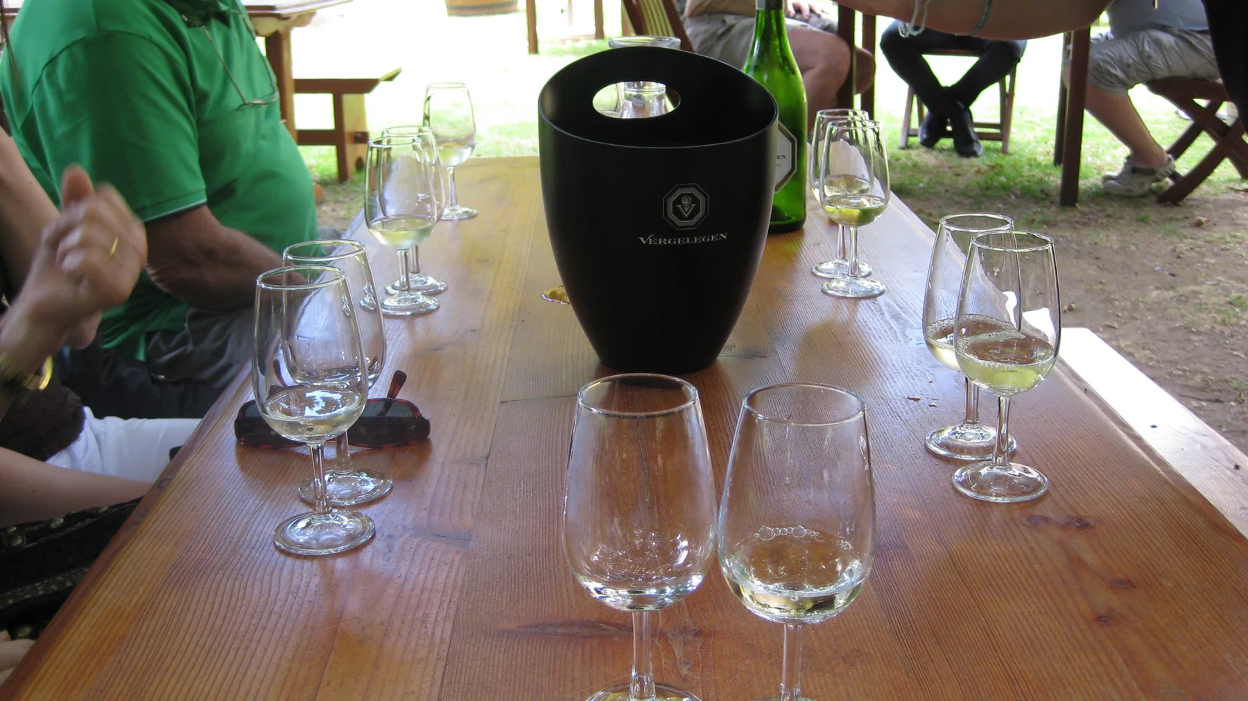 Several glasses and a dark container sit on a wooden tasting table.