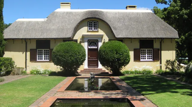 A narrow reflecting pool leads toward a thatched house entrance.
