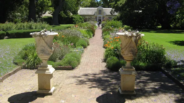 Two stone urns flank a straight path toward a thatched building.