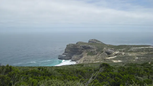 A rocky cape projects into blue water beyond green slopes.