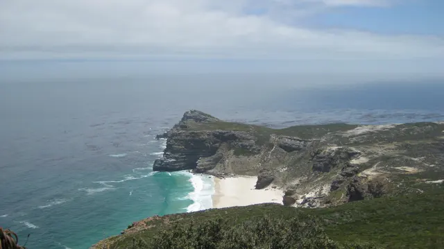 A small pale beach lies beneath steep coastal cliffs.