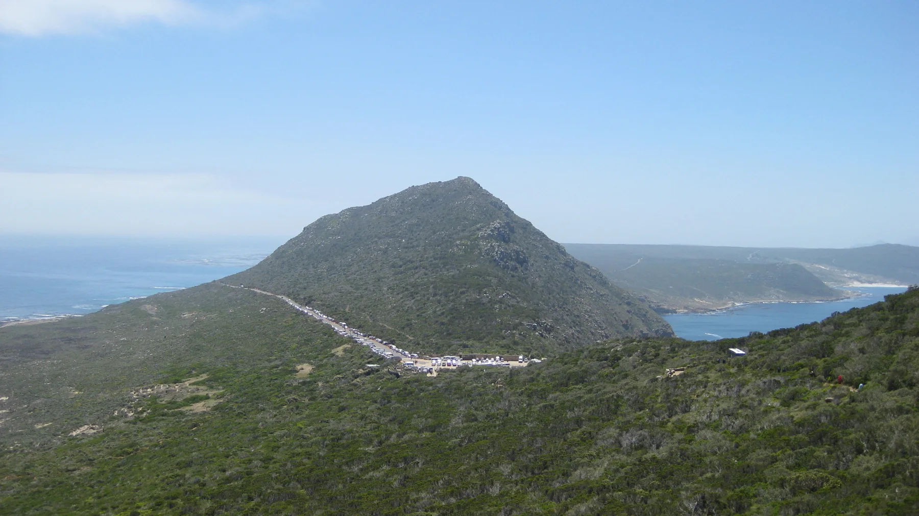 A winding road crosses a rounded hill above the sea.