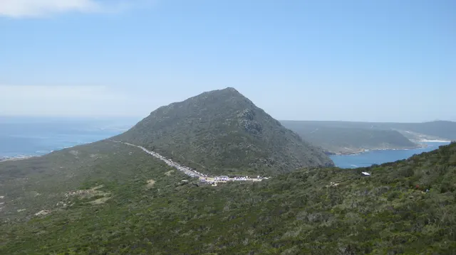 A winding road crosses a rounded hill above the sea.