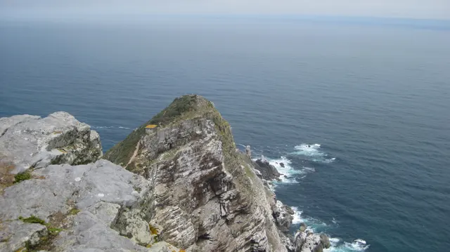 A narrow rocky point drops toward calm dark blue sea.