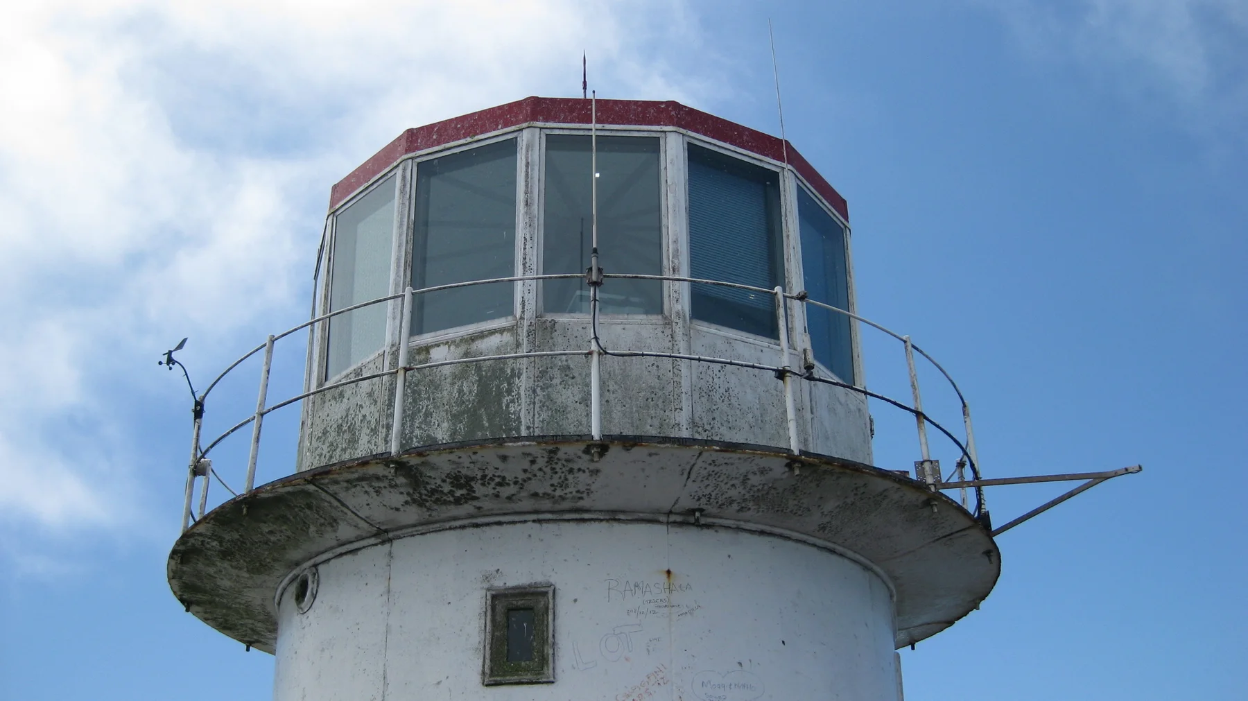 A weathered lighthouse lantern sits above a white tower.