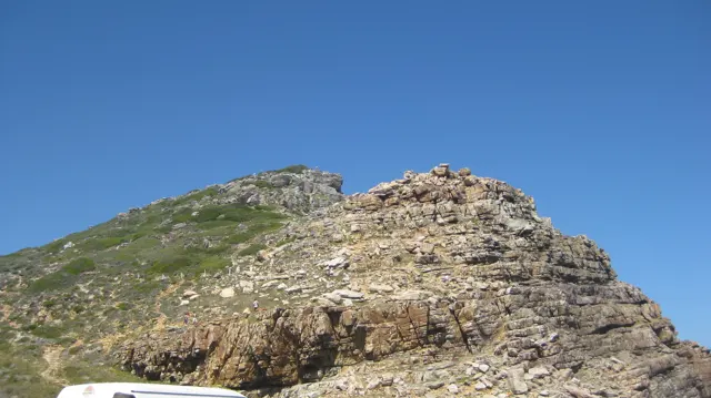 A rugged rock ridge rises above a green slope.