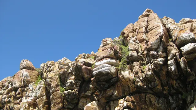 Jagged brown rocks stand against clear blue sky.