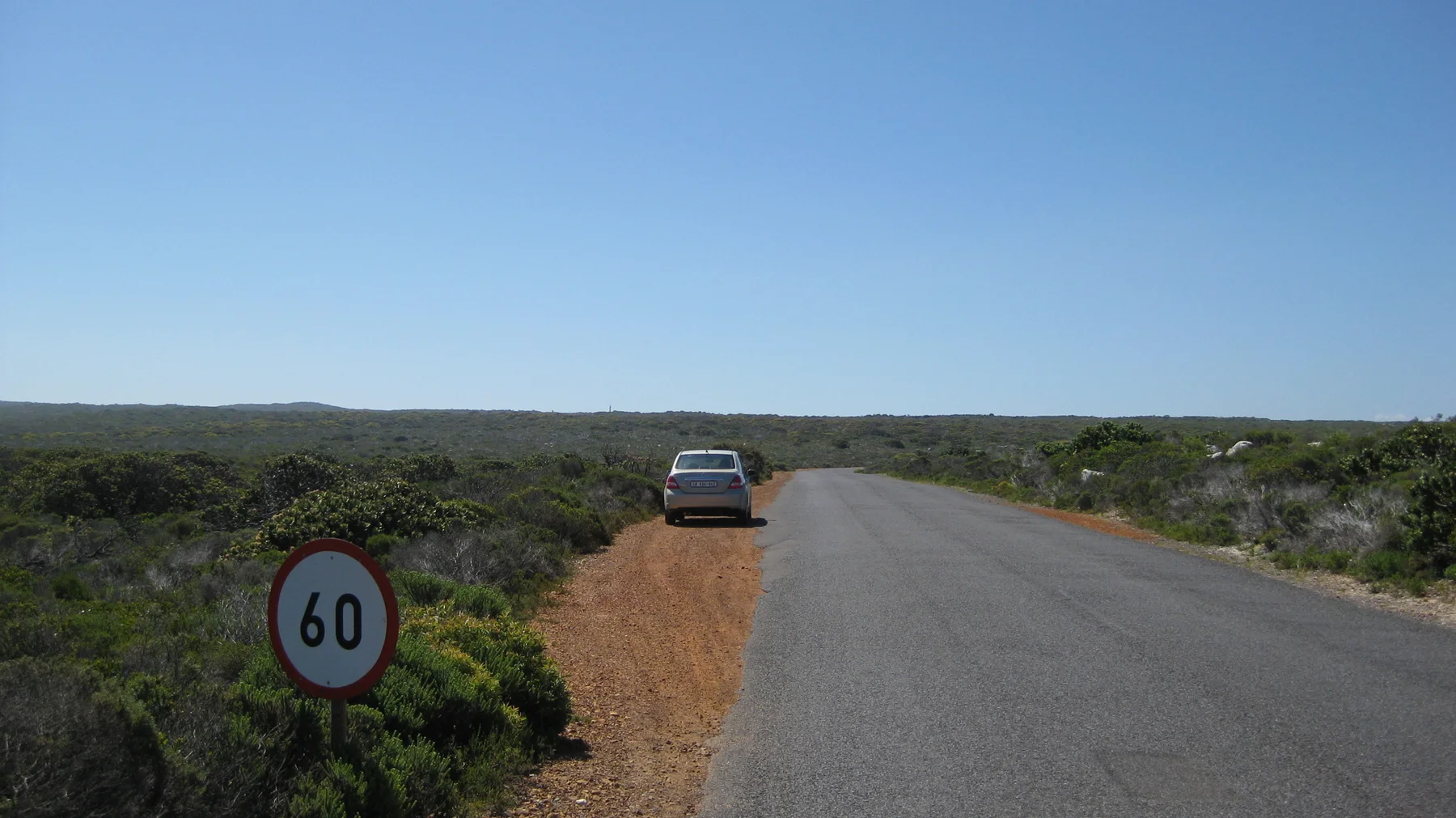 A car stands on a sandy verge near a sixty-speed sign.