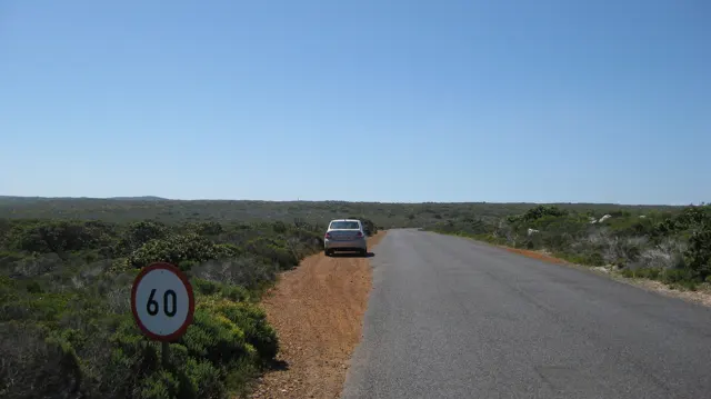 A car stands on a sandy verge near a sixty-speed sign.
