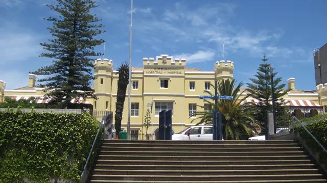Wide steps lead toward an ornate yellow building and tall trees.