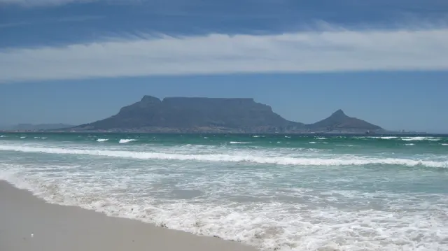 White waves break beneath a distant flat-topped mountain.