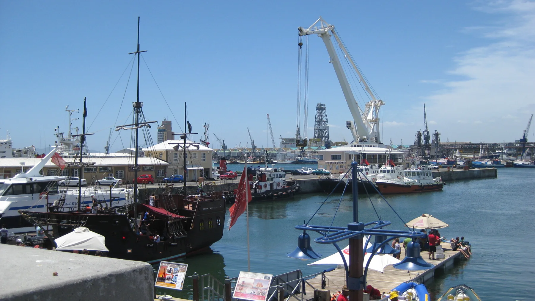 Boat masts and a large crane rise above calm harbor water.