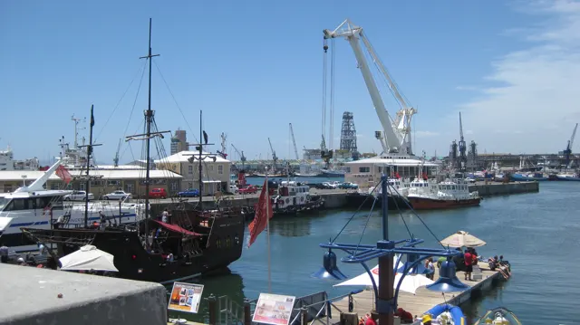 Boat masts and a large crane rise above calm harbor water.