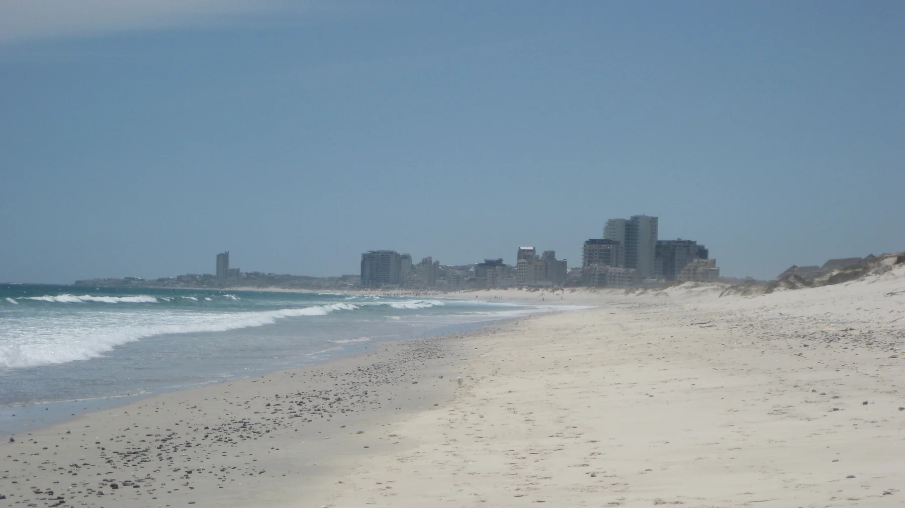 A long sandy beach leads toward distant waterfront towers.