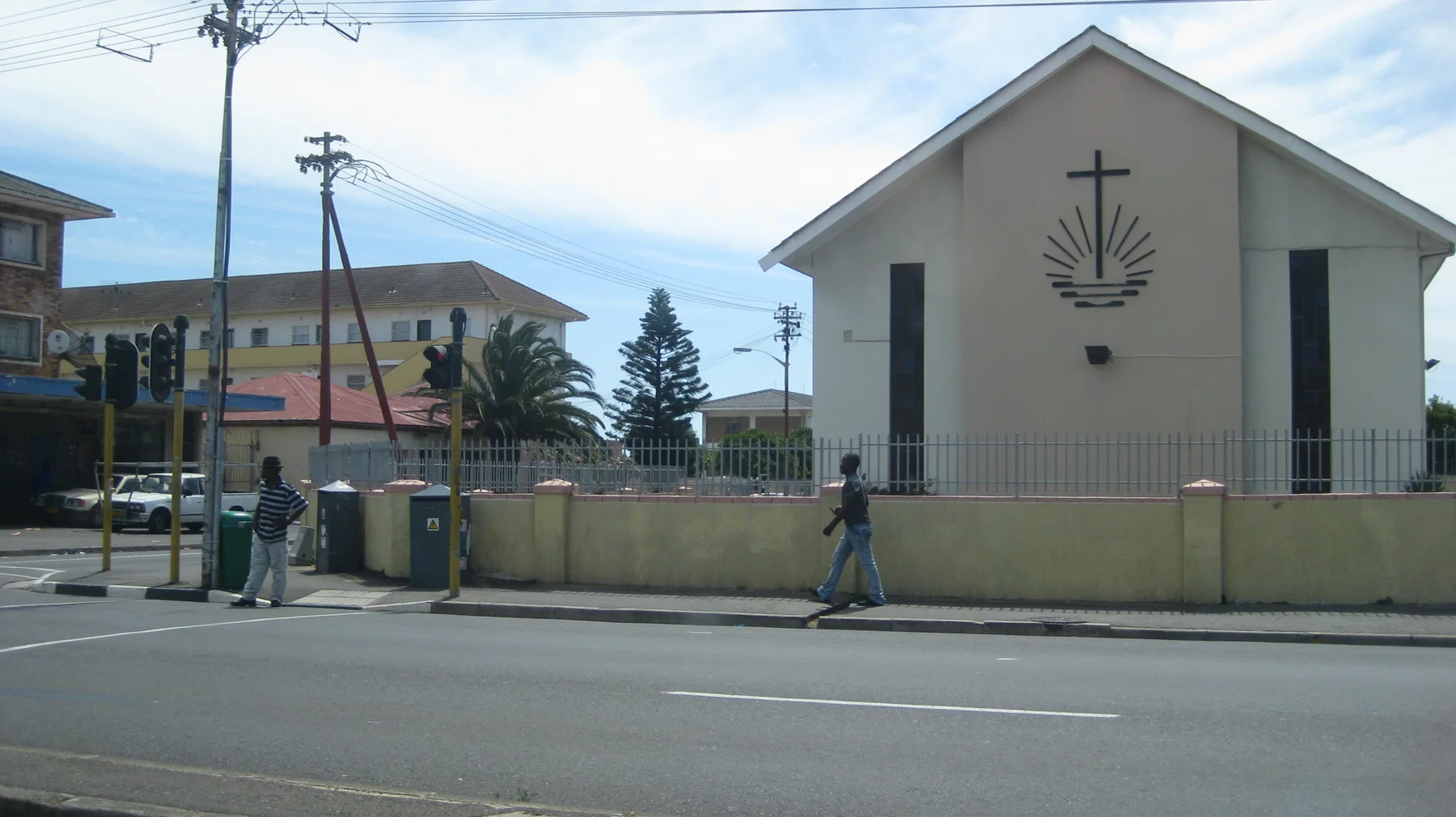 A pale church facade bears a cross beside a busy street.