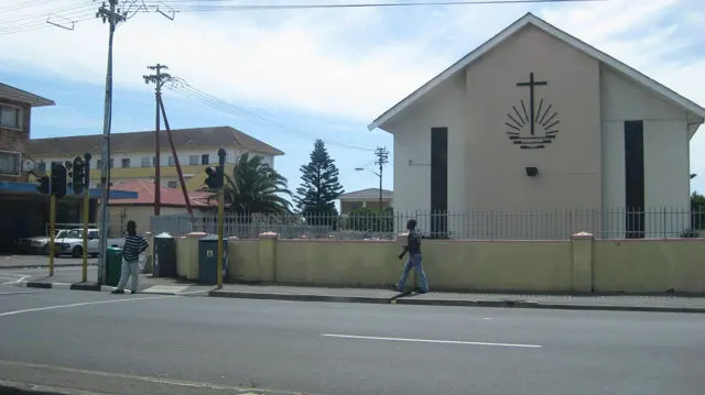 A pale church facade bears a cross beside a busy street.