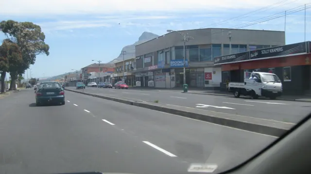 Low shops line a wide road with passing vehicles.
