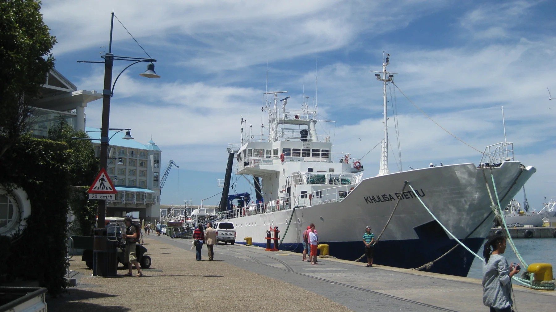 A large white ship is moored beside a pedestrian quay.