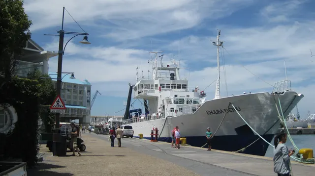 A large white ship is moored beside a pedestrian quay.