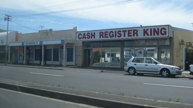 A storefront marked Cash Register King faces a parked car.