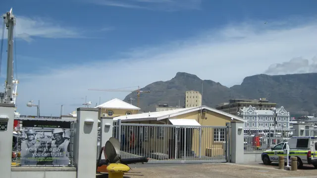 Small harbor buildings and railings stand below a mountain backdrop.