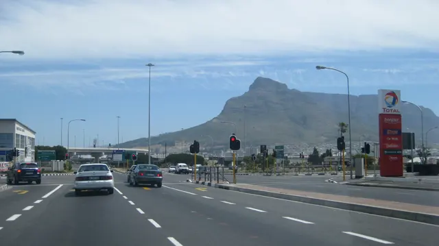 Several cars approach traffic lights beneath a pointed mountain.