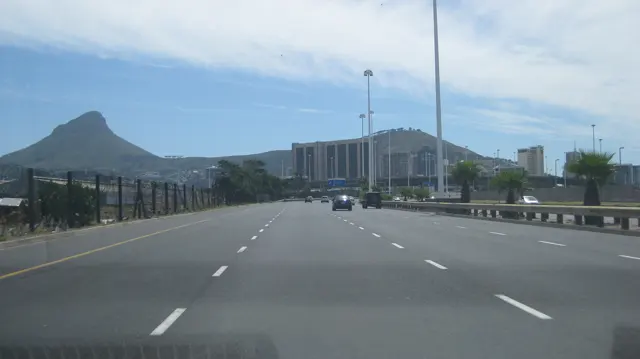 An open road leads toward tall buildings below a pointed hill.