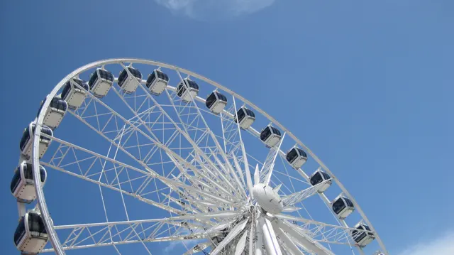 The upper arc of an observation wheel rises against blue sky.