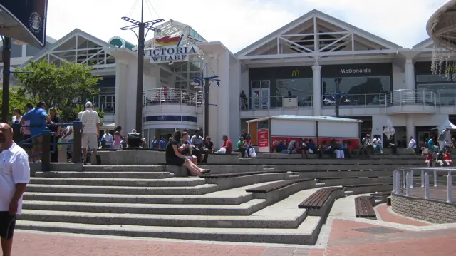 People sit and walk on broad steps outside a waterfront building.