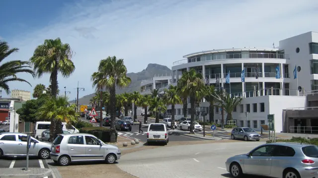 Palms and cars stand before a curved white commercial building.