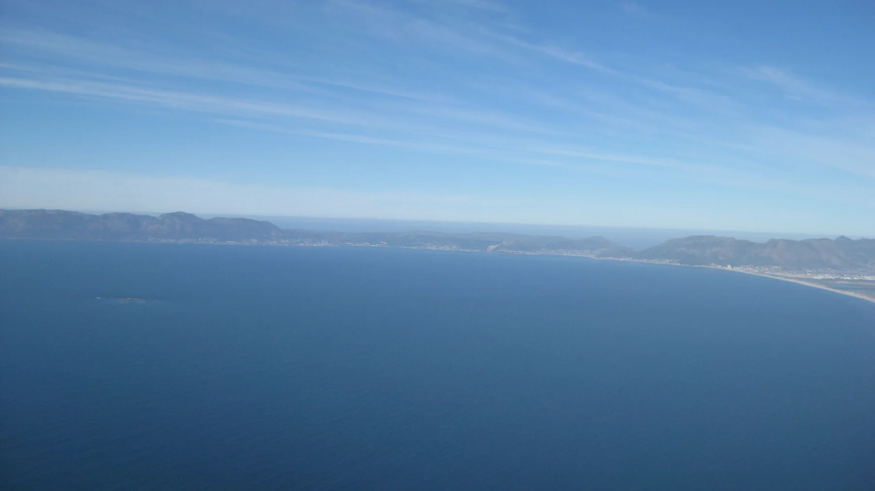 A long coastline curves around blue ocean in an elevated view.