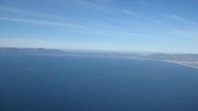 A long coastline curves around blue ocean in an elevated view.