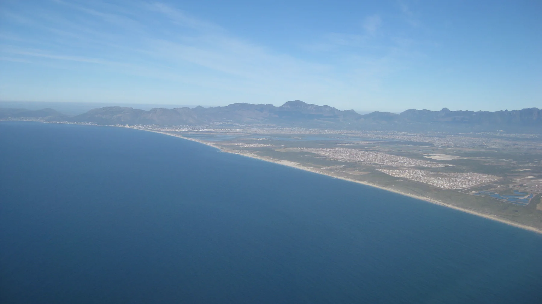 A broad bay curves below distant mountains in an aerial view.