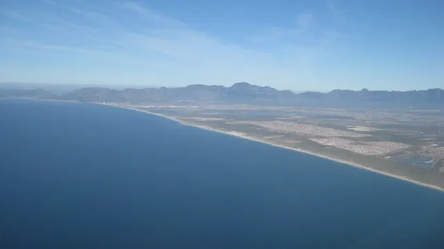 A broad bay curves below distant mountains in an aerial view.