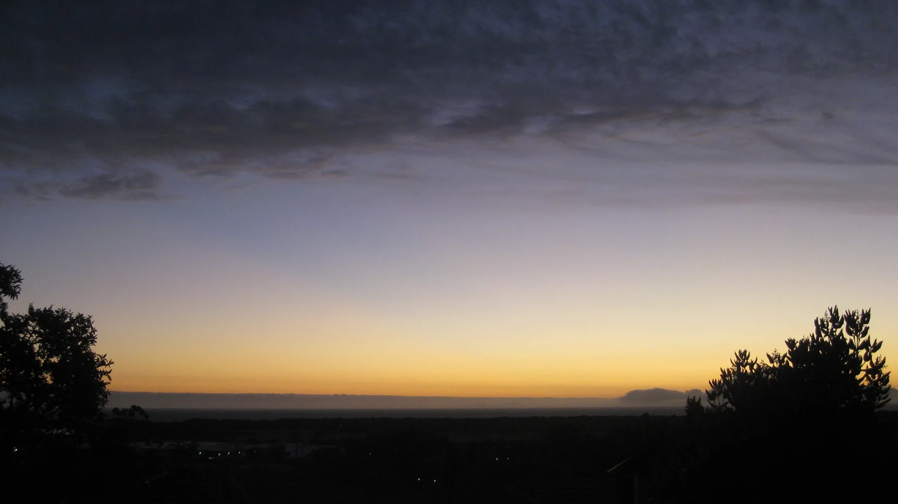 A thin golden horizon glows below dark twilight clouds.