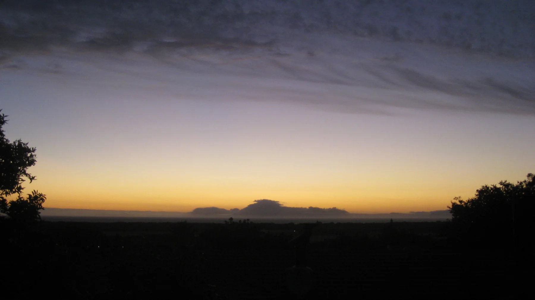Dark trees frame a low orange band beneath a purple-gray sky.