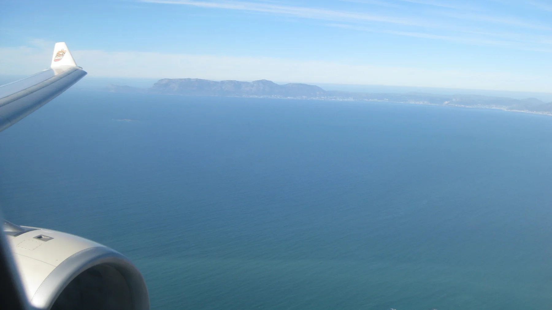 An aircraft wing and engine frame blue water and distant land.