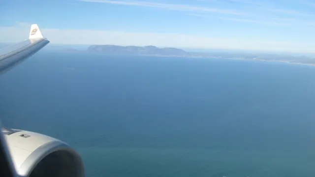 An aircraft wing and engine frame blue water and distant land.
