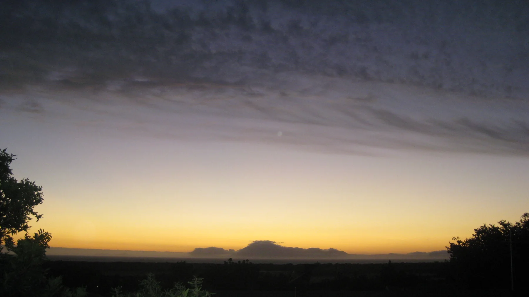 A pale golden band separates dark land from dusk clouds.