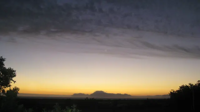 A pale golden band separates dark land from dusk clouds.