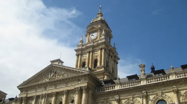 An ornate stone clock tower rises above a columned city facade.