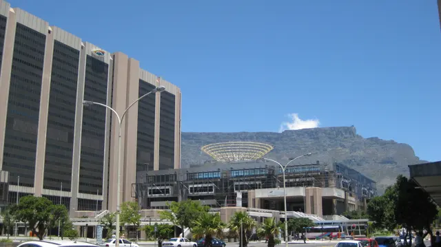 Tall office blocks stand beside a modern structure beneath a mountain.