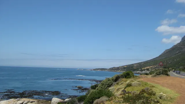 A sandy pullout overlooks calm water beside a green coastal slope.