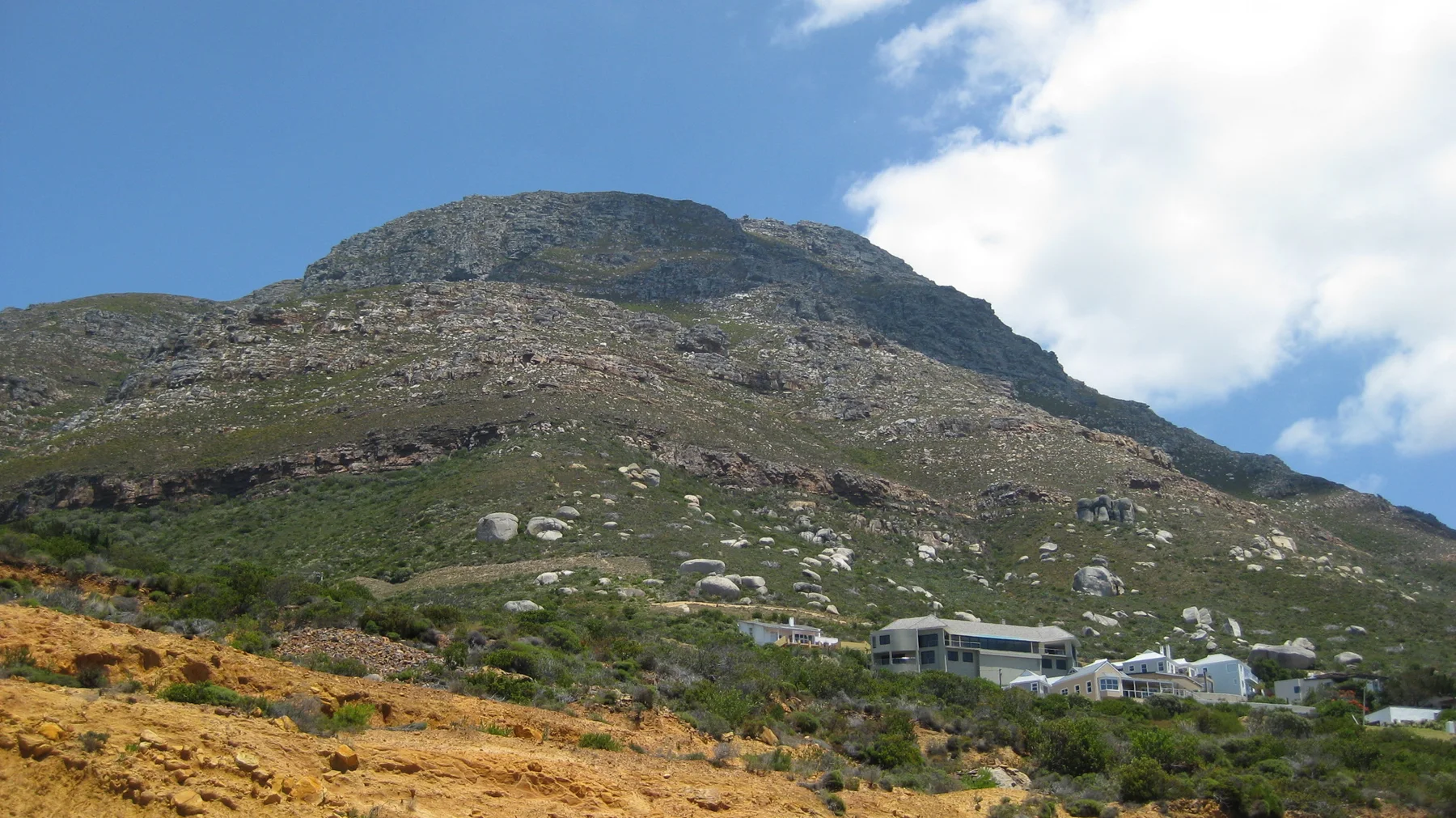 A rounded rocky hill rises above low hillside houses.