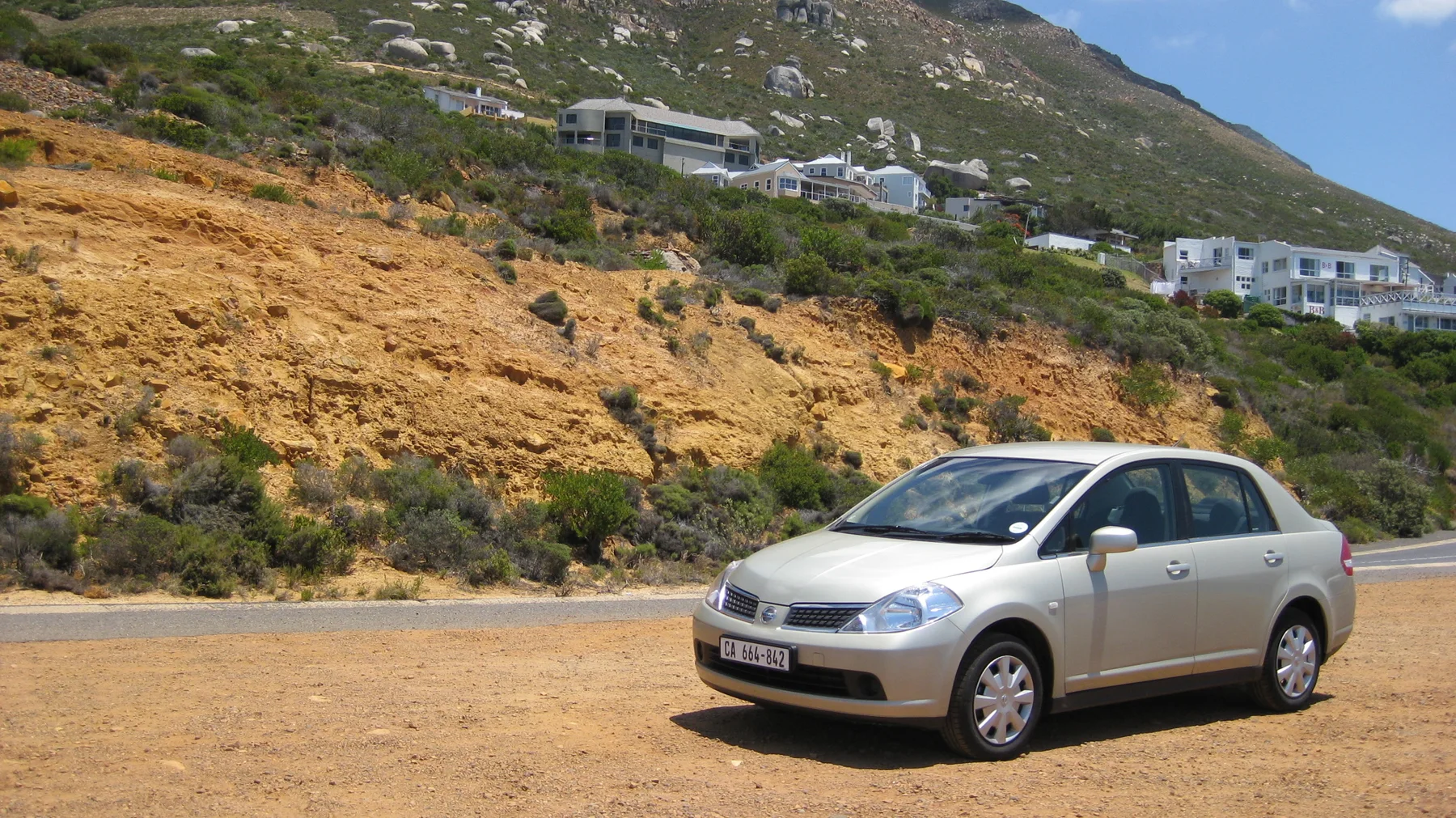 A white car stands on gravel below an ochre roadside bank.