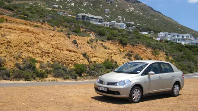A white car stands on gravel below an ochre roadside bank.