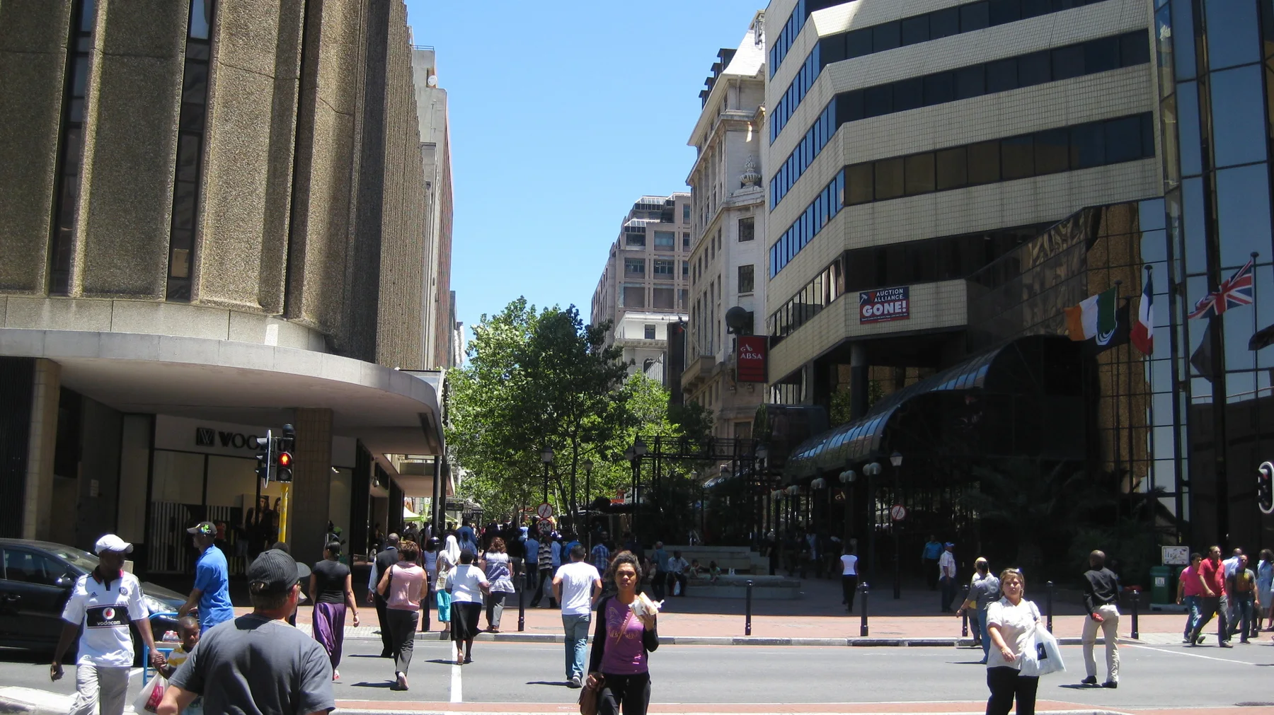 Pedestrians cross a busy street between tall city buildings.