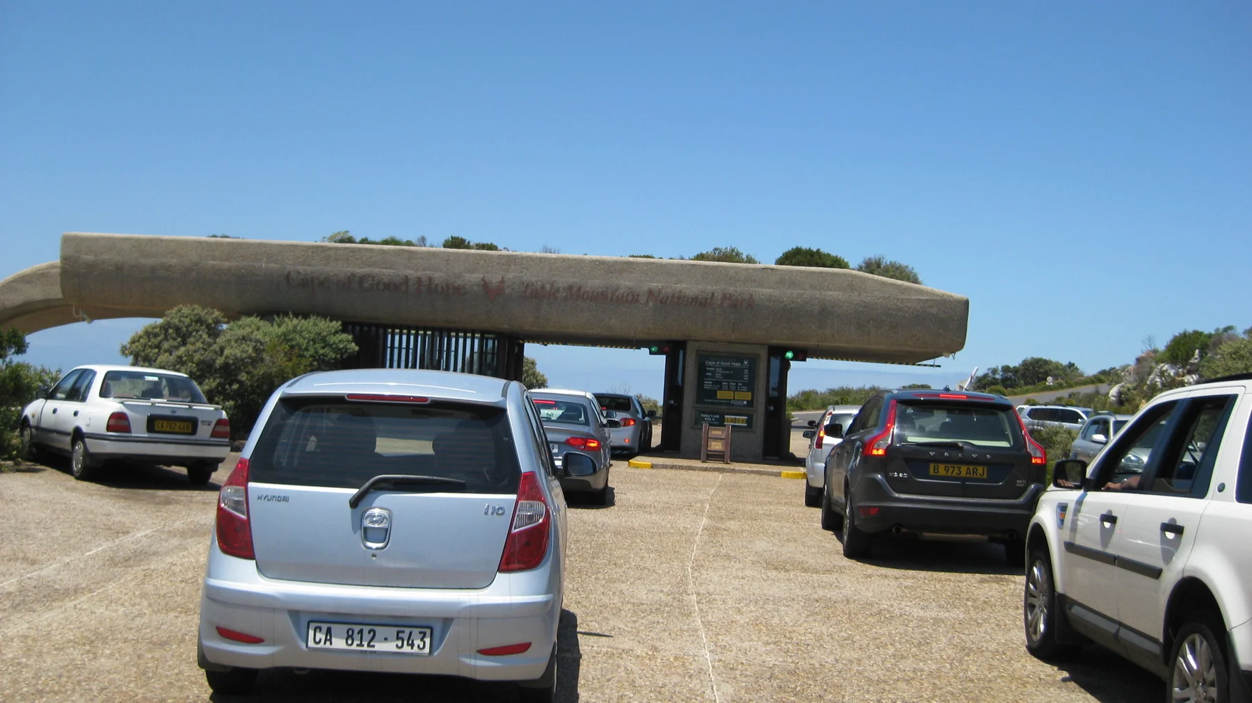 Vehicles wait beside entrance booths under a wide canopy.