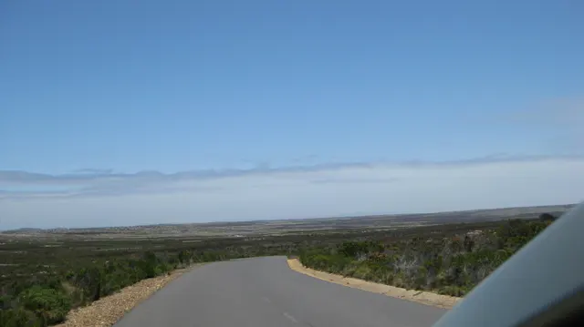 A paved road descends through low coastal scrub.